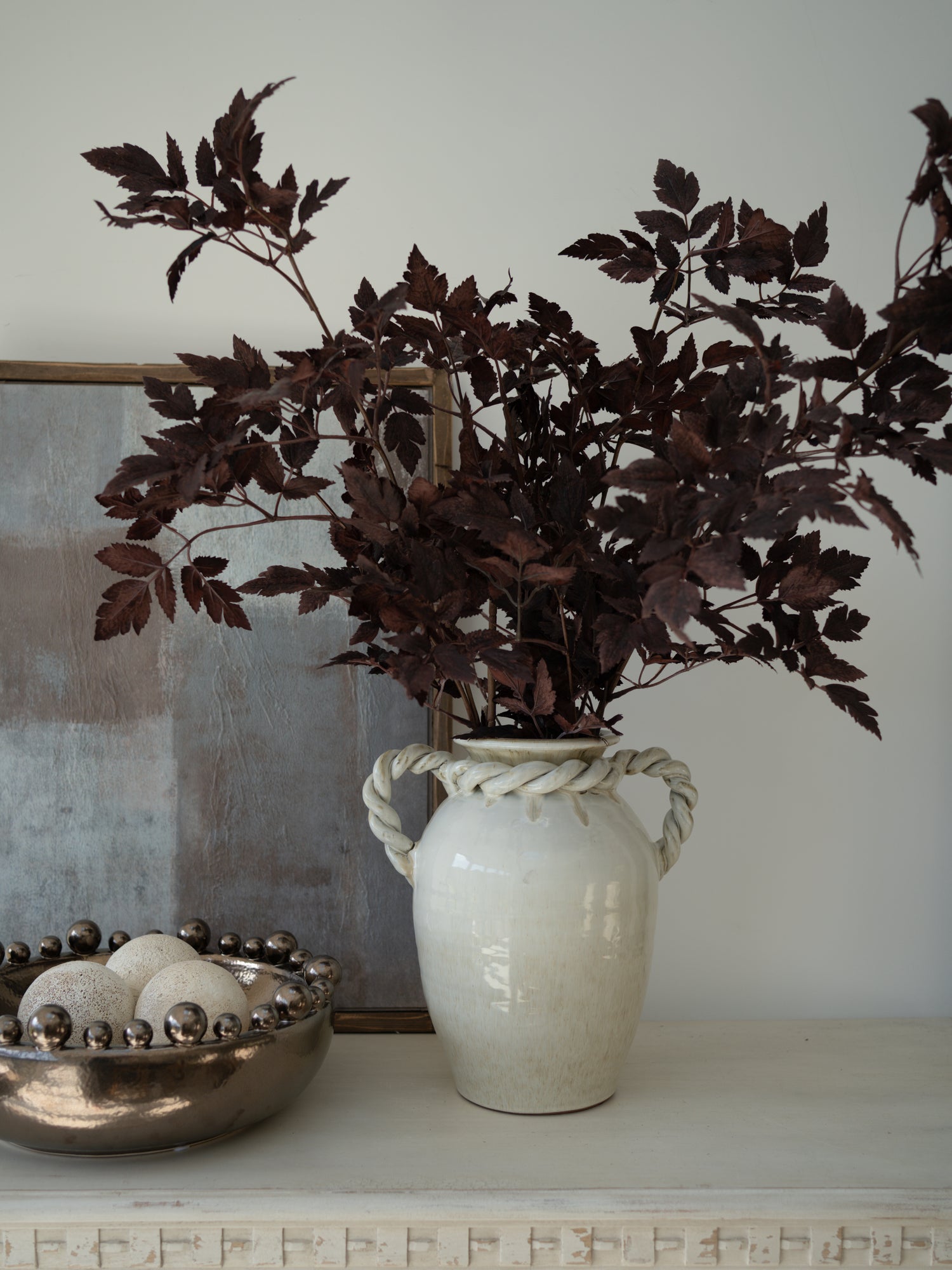 White vase with Faux Burgundy Physocarpus Diablo on a surface with a neutral background