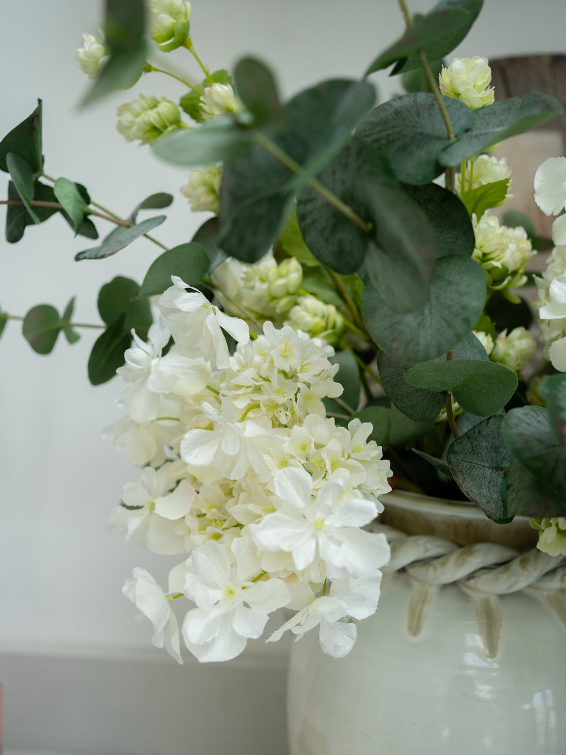 Faux white butterfly hydrangea and green leaves in a woven basket against a light background