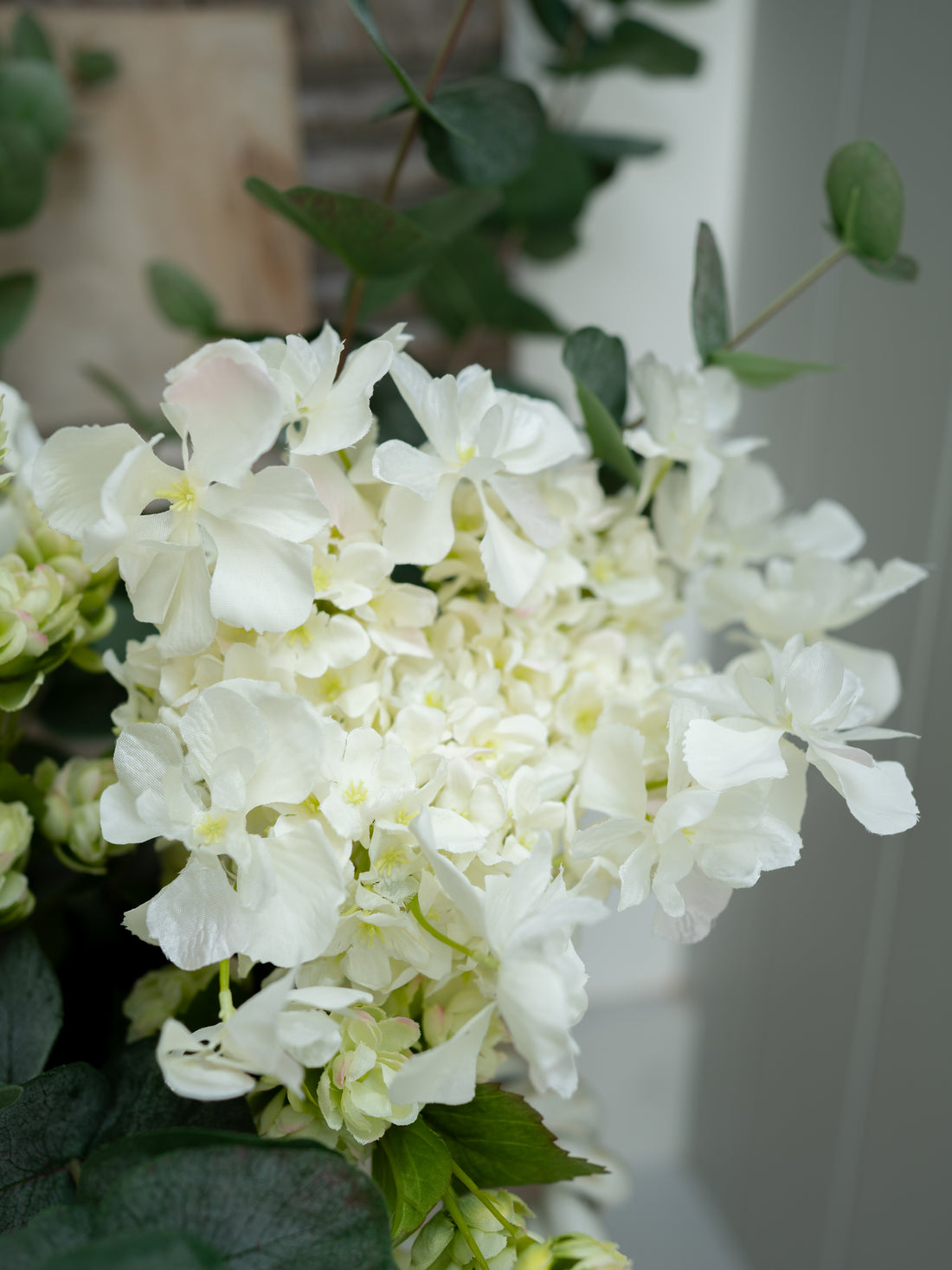 Close-up of faux white butterfly hydrangea with green leaves on a blurred background