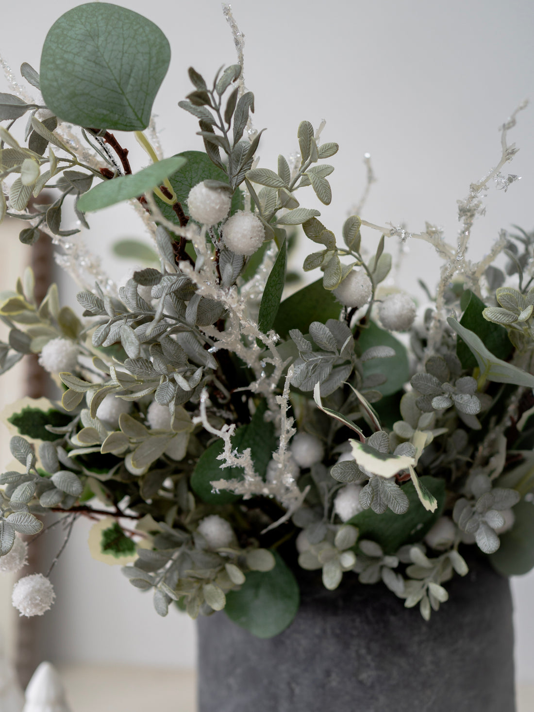Decorative arrangement of faux christmas greenery and white berries in a gray vase against a neutral background