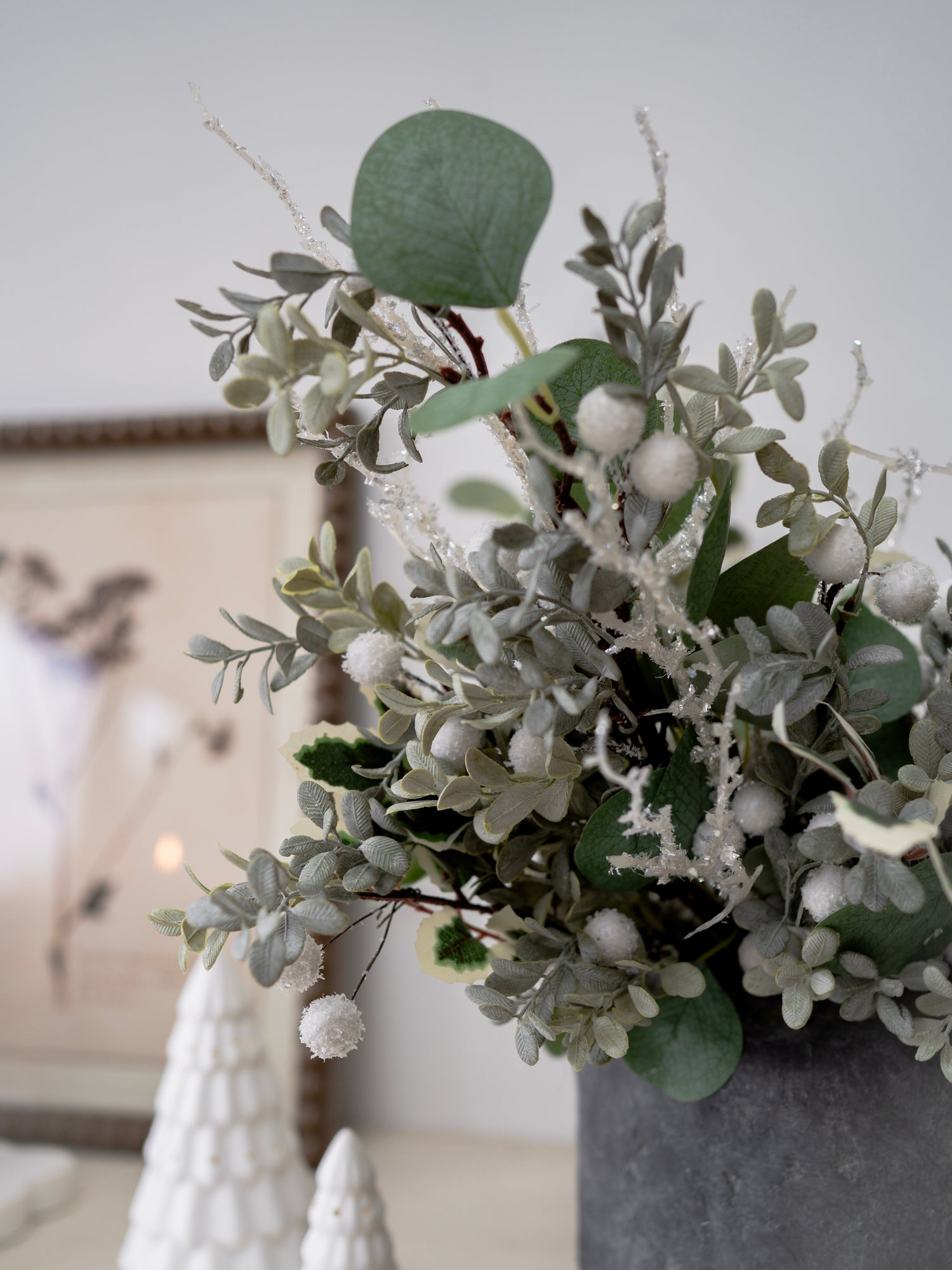 Decorative arrangement of faux christmas greenery and white berries in a vase on a neutral background