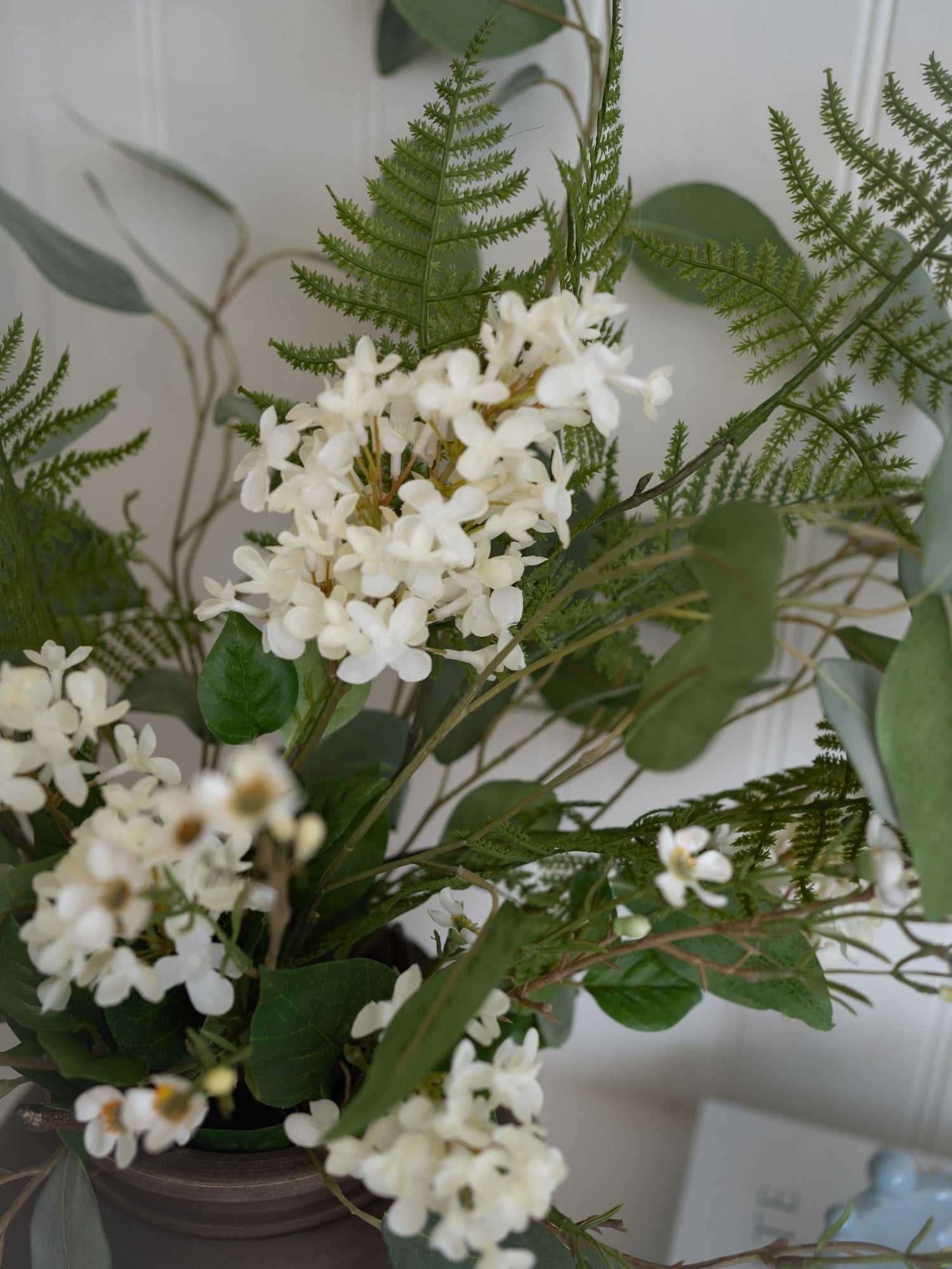 Artificial white floral arrangement with white flowers and green leaves on a neutral background