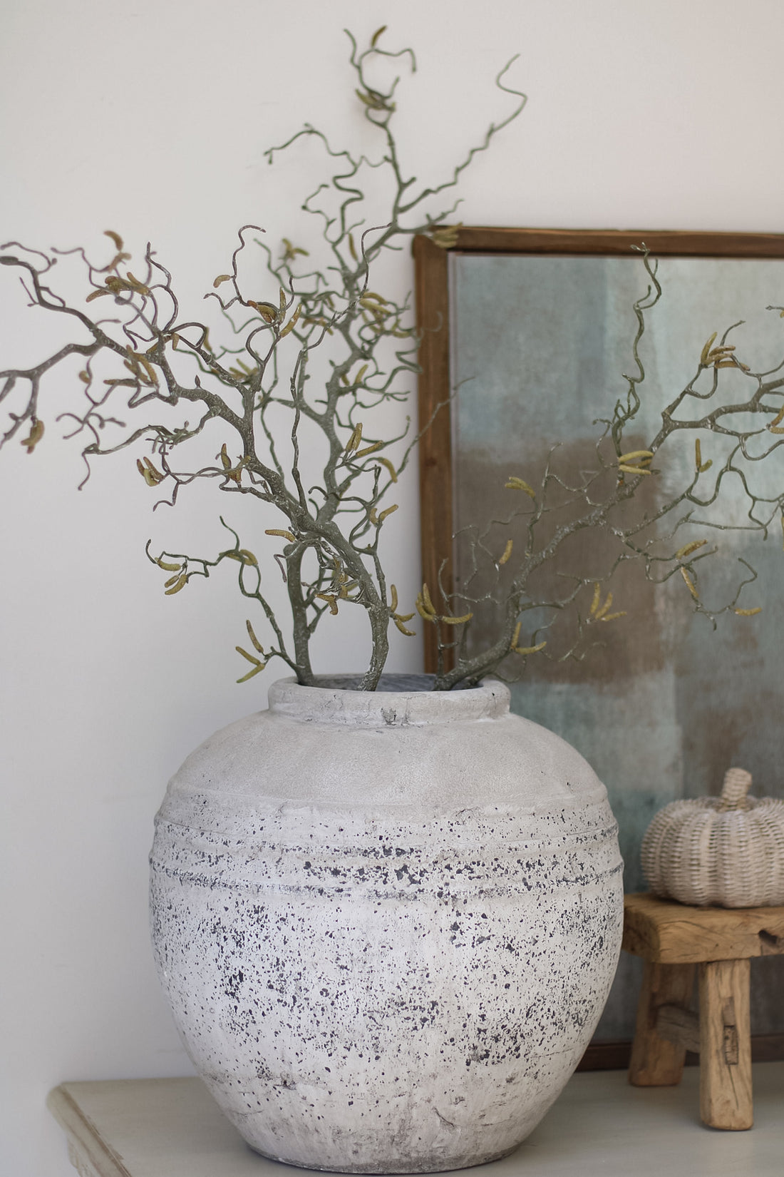 Decorative vase with branches on a shelf against a white wall