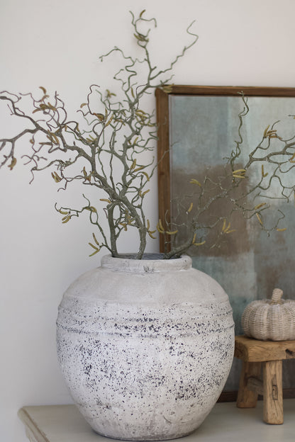 Decorative vase with branches on a shelf against a white wall