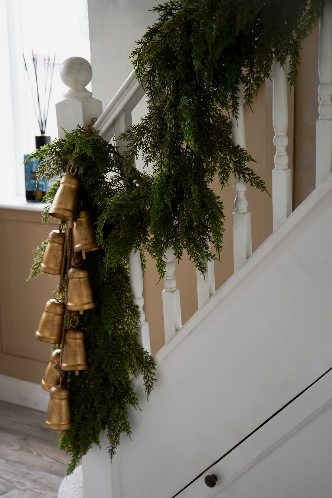 Decorative faux green cypress garland with gold bells on a staircase
