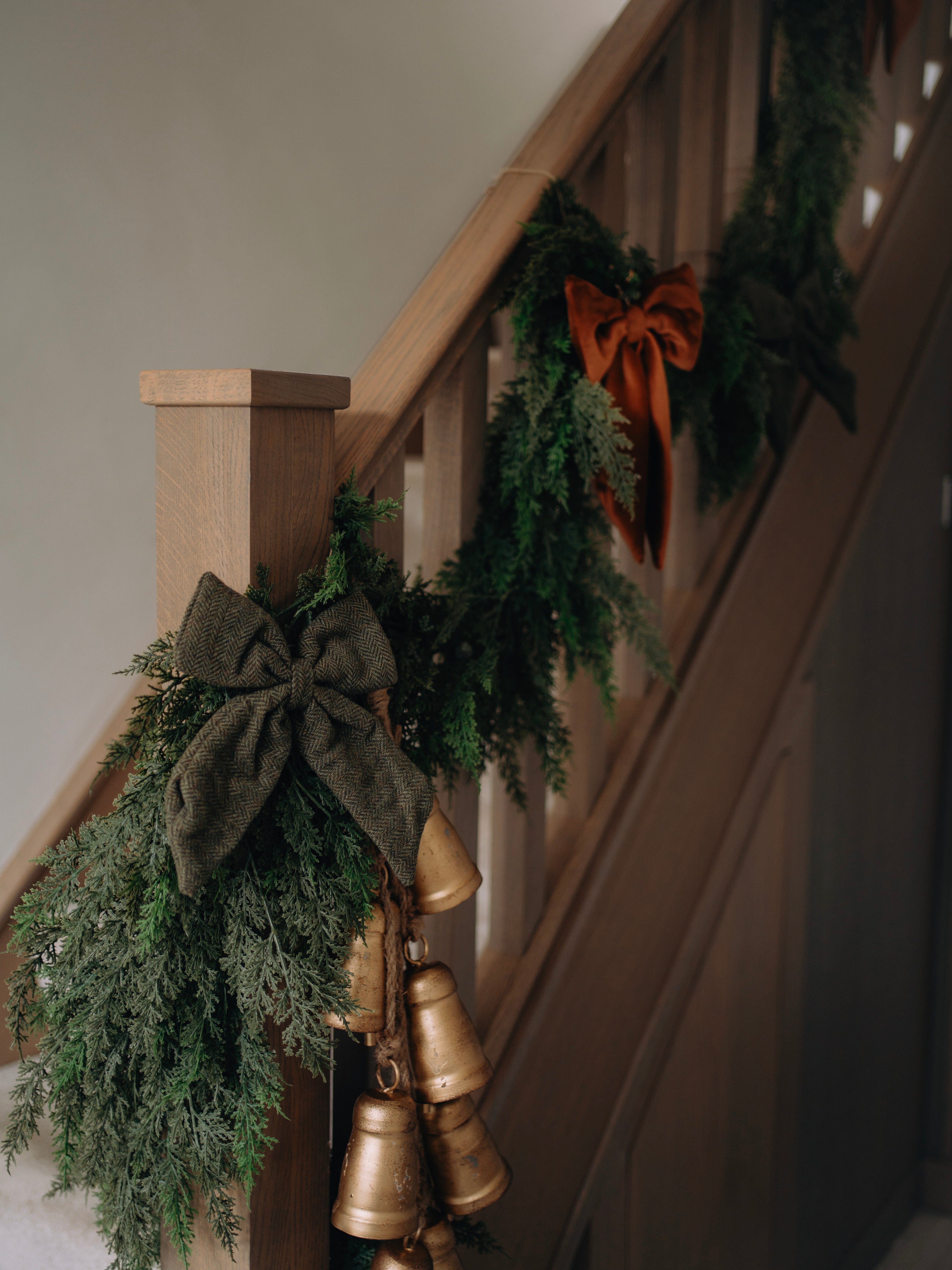 Decorative faux greenery garland with gold bells and ribbons on a staircase.