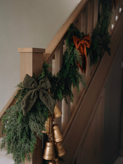 Decorative faux greenery garland with gold bells and ribbons on a staircase.