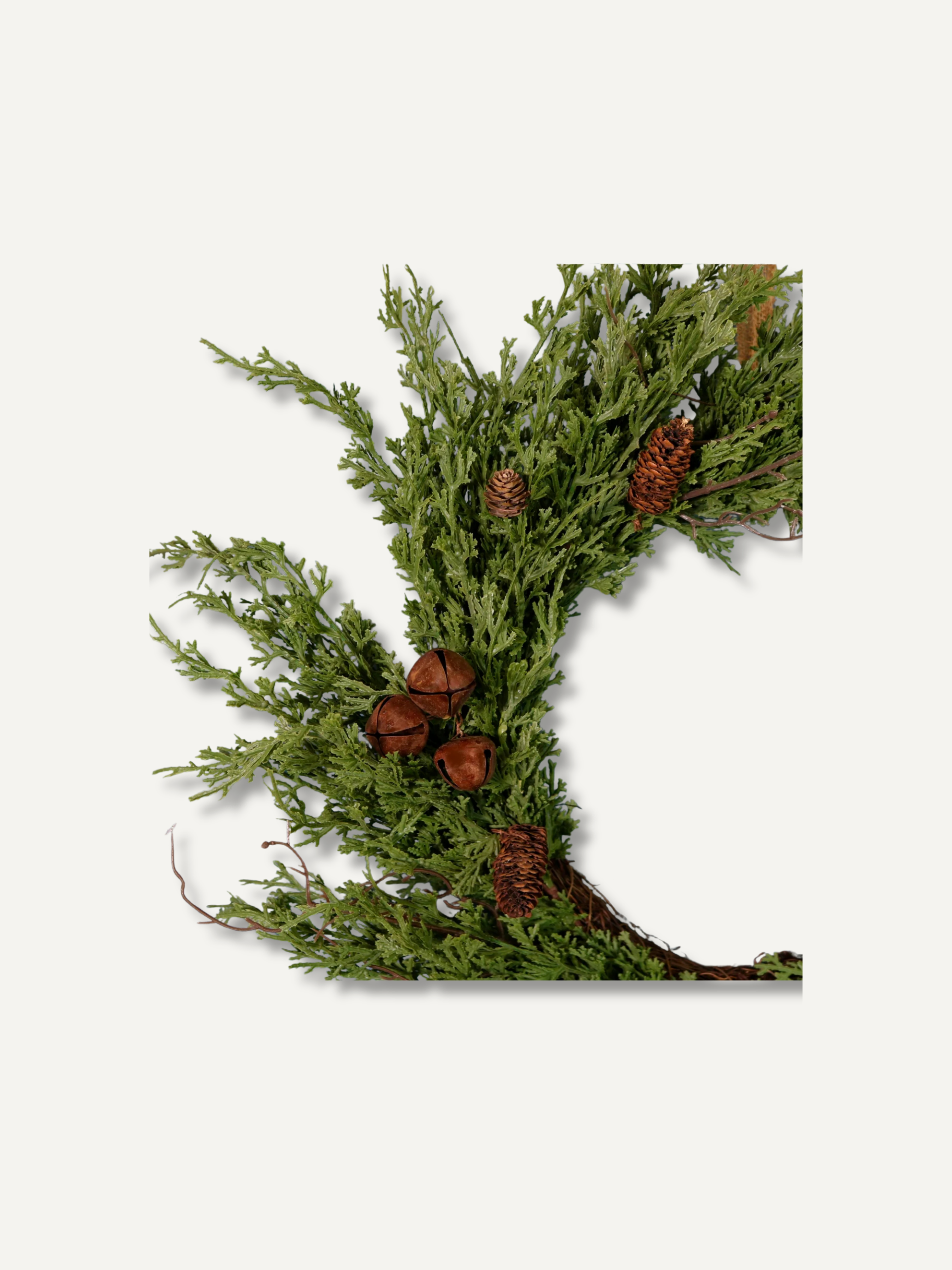 A decorative artificial green evergreen wreath with small brown pinecones and acorns, photographed against a plain light gray background.
