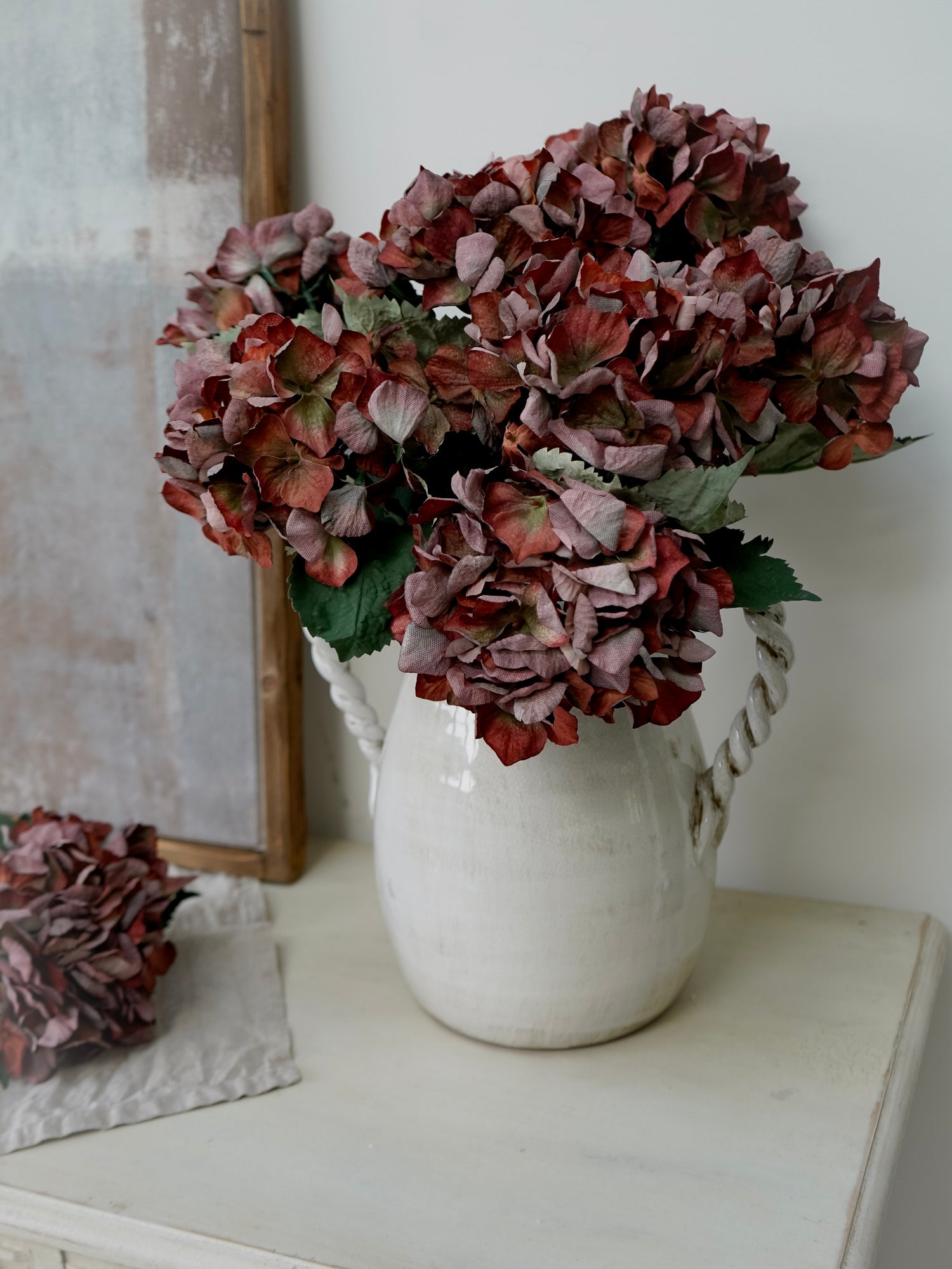 White vase with dried red and green hydrangeas on a white surface