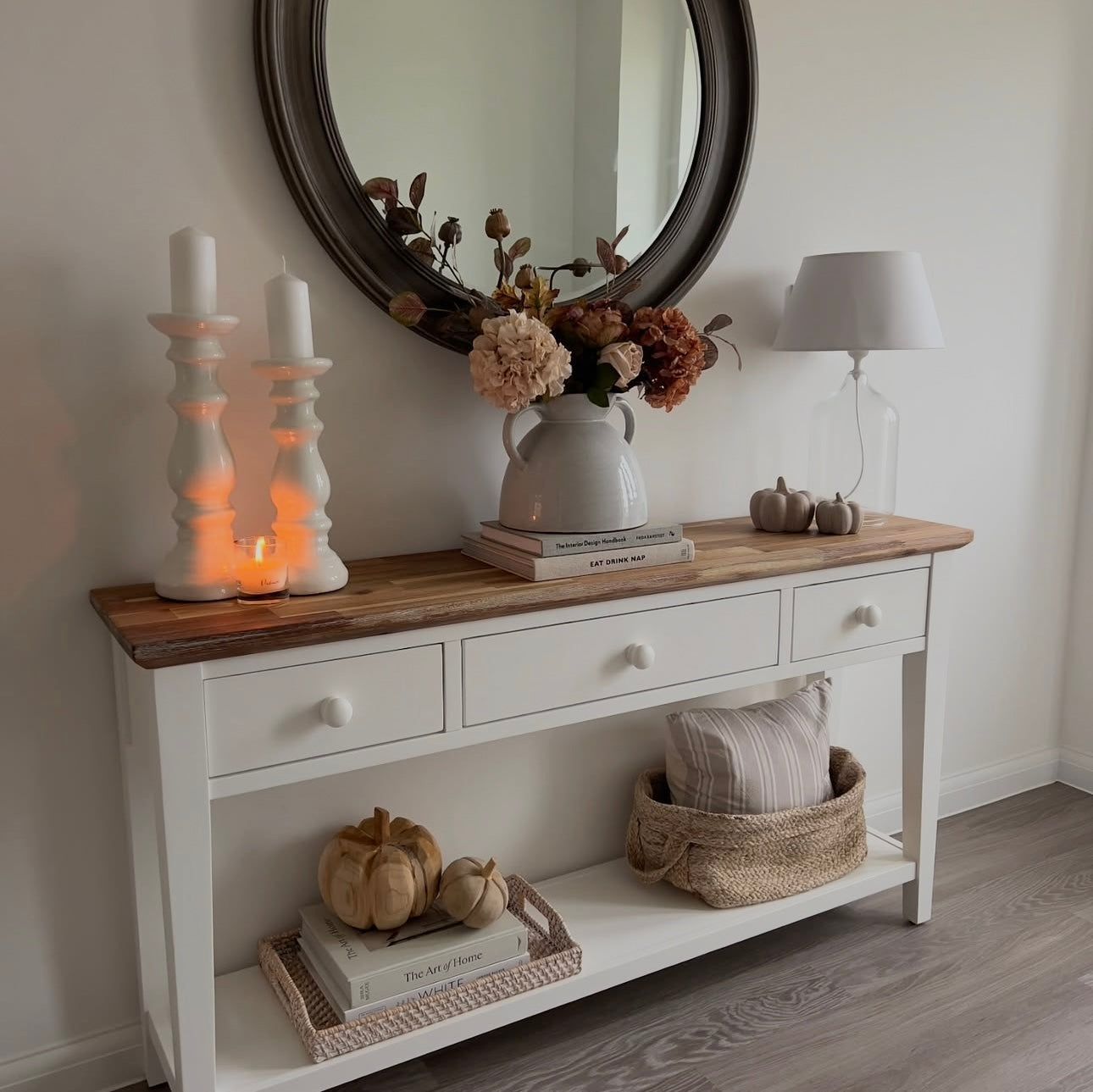 Hallway table styled with tall pillar candles, vase filled with faux dried hydrangea, lamp and small pumpkins