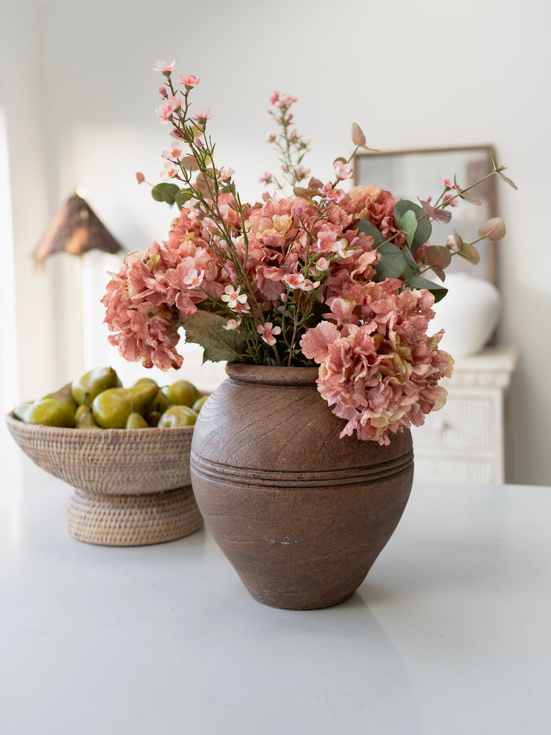 Terracotta vase with pink faux flower arrangement on a white surface