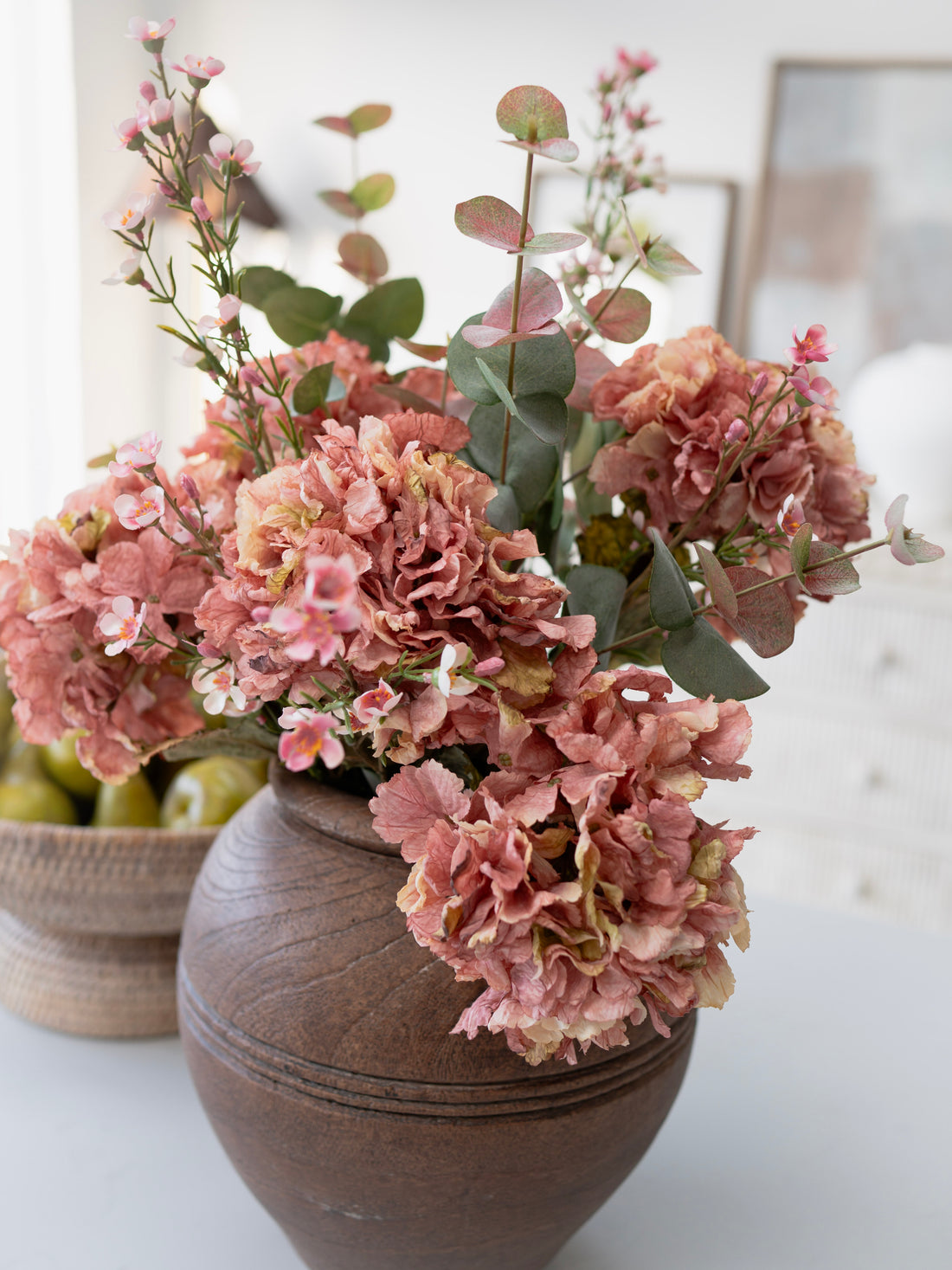 Decorative vase with faux pink flowers and eucalyptus on a light background