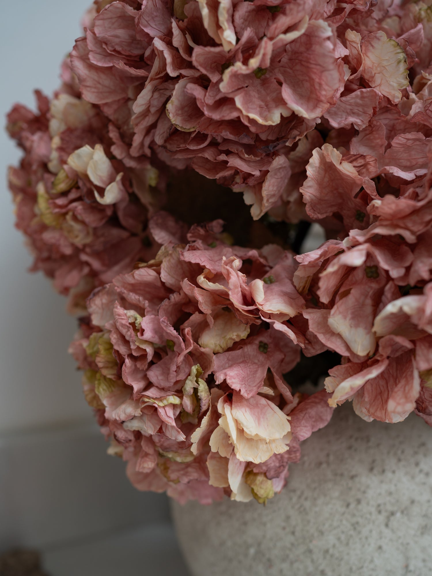 Close-up of faux pink hydrangeas in a white vase on a light background