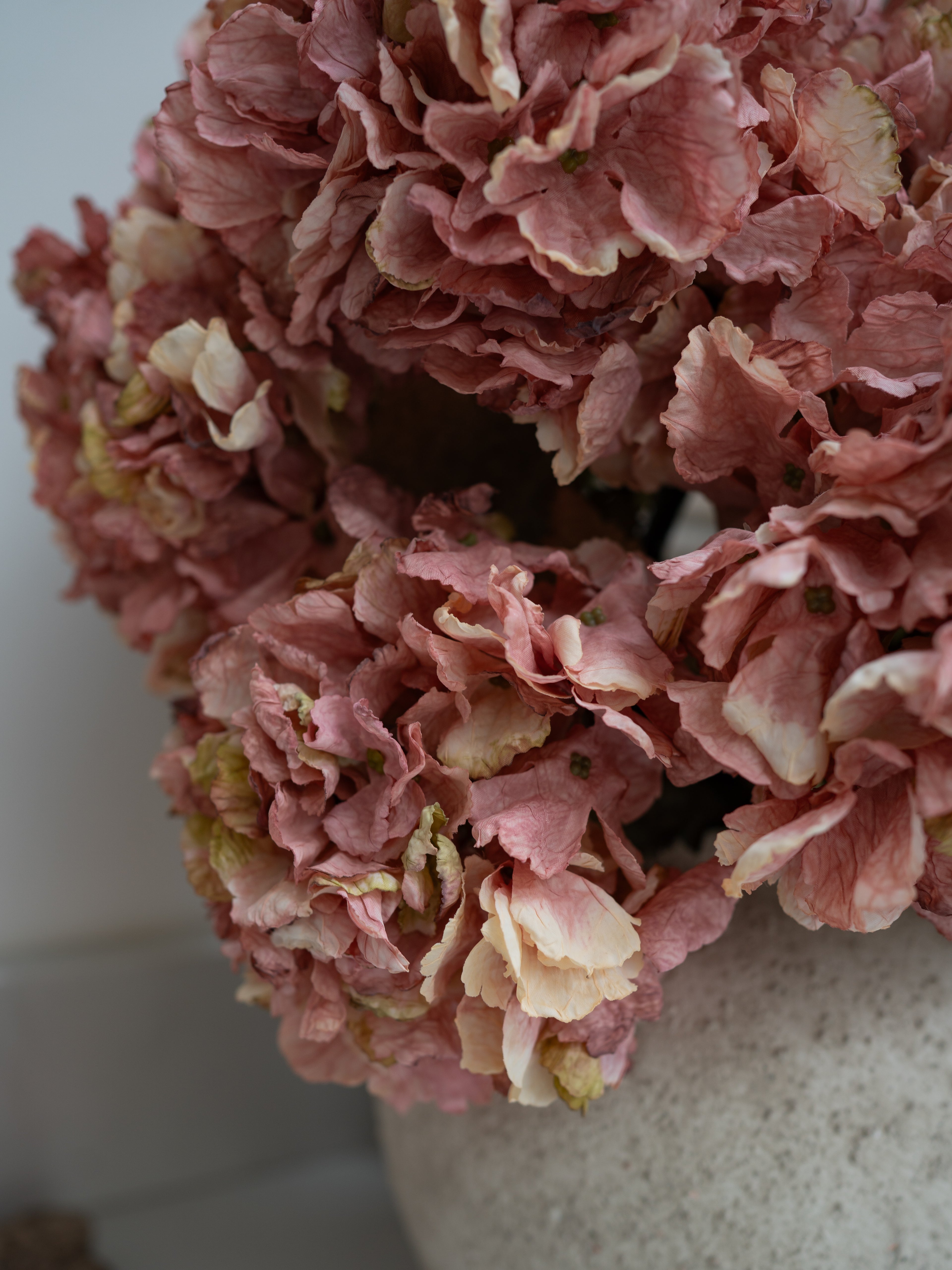 Close-up of faux pink hydrangeas in a white vase on a light background
