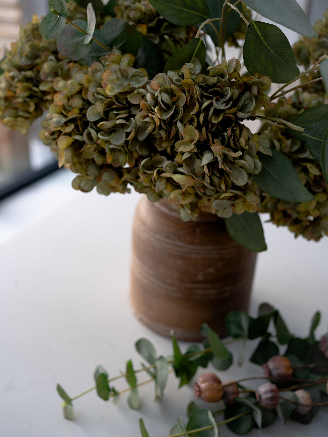 Bouquet of dried hydrangeas in a brown vase on a white surface