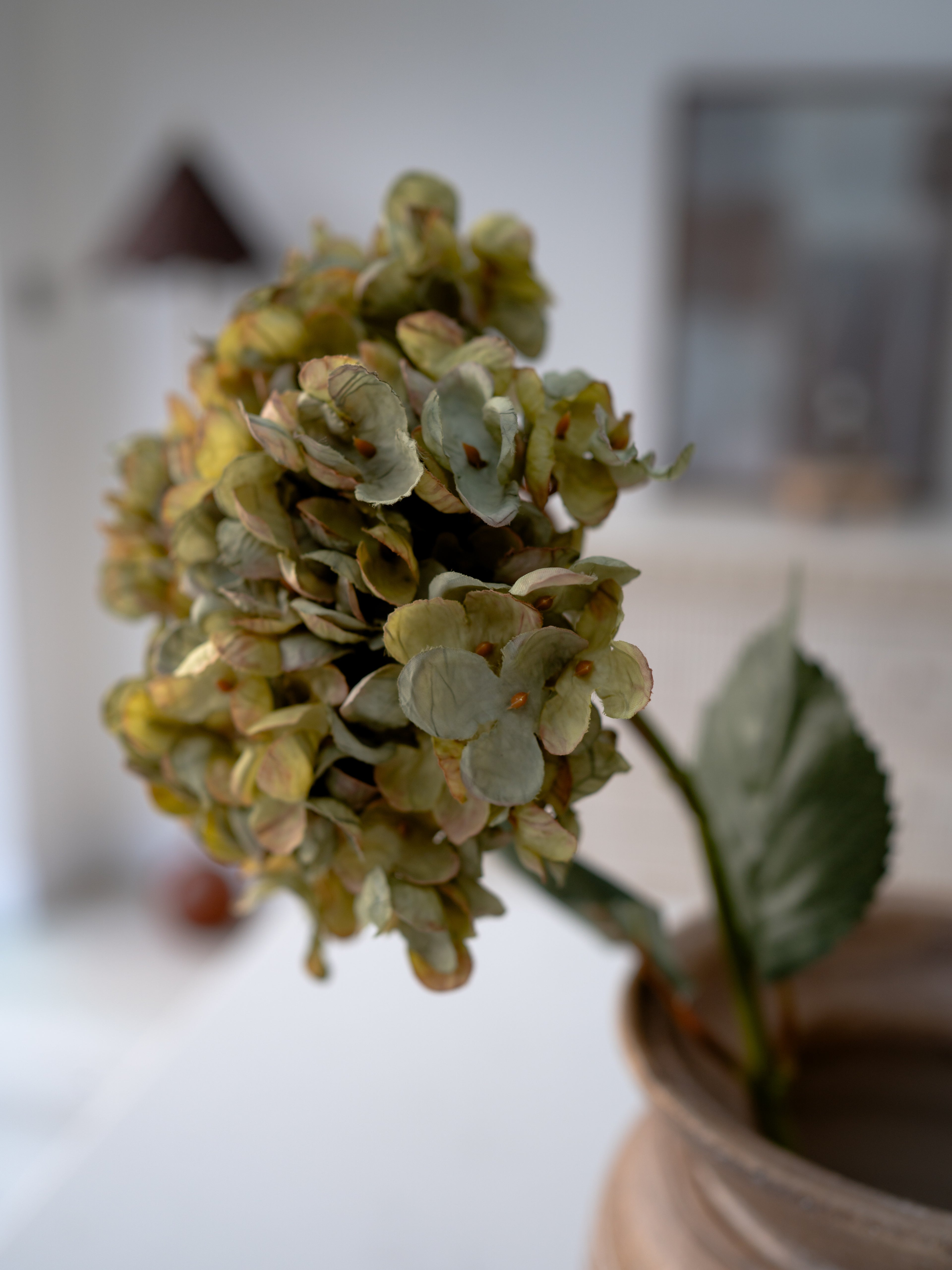 Artificial green hydrangea flower arrangement in a pot on a blurred background