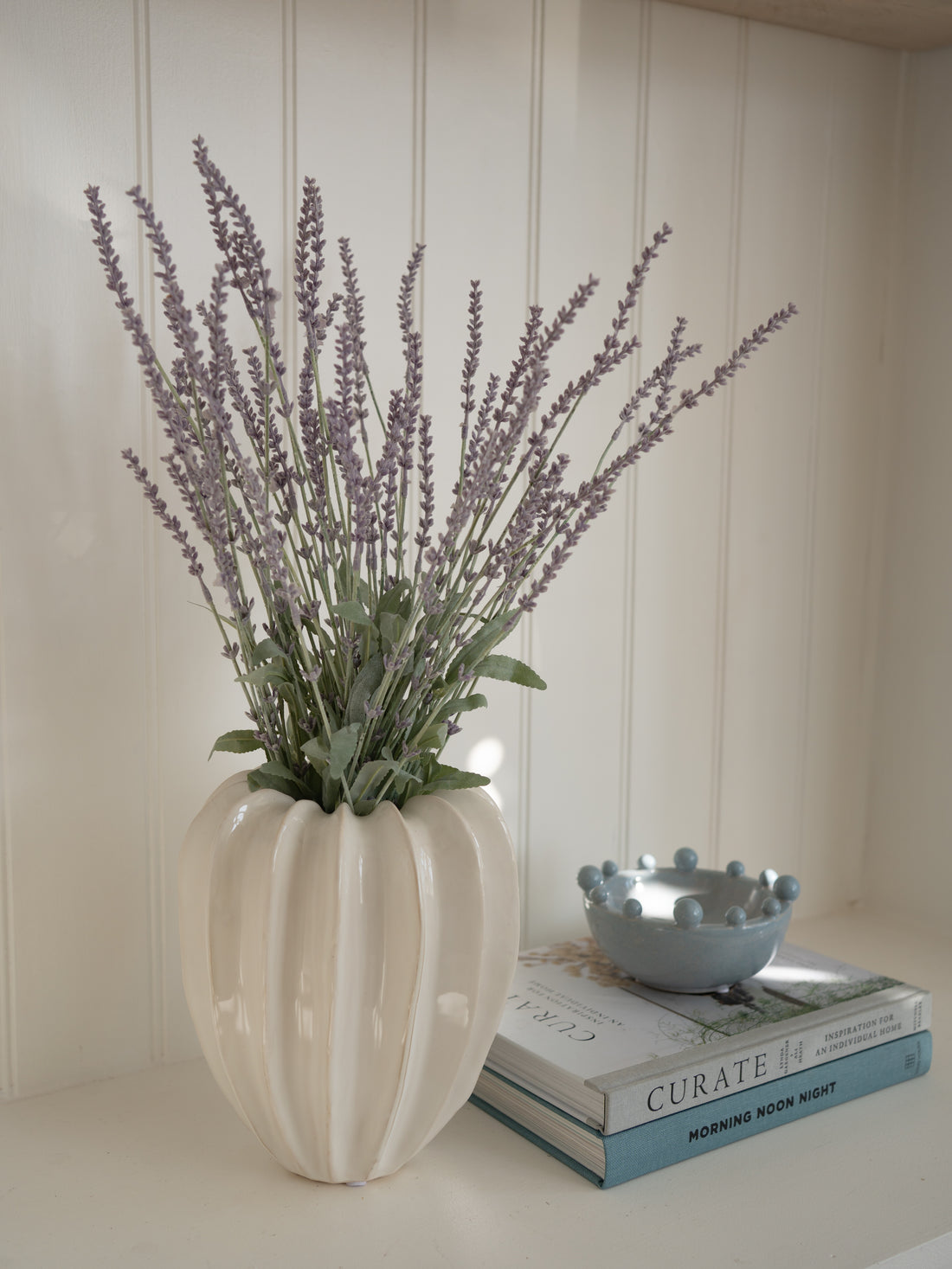 Decorative vase with faux lavender on a surface with books and a bowl.