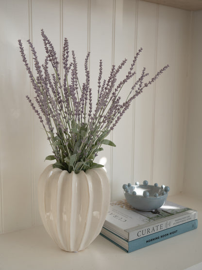 Decorative vase with faux lavender on a surface with books and a bowl.