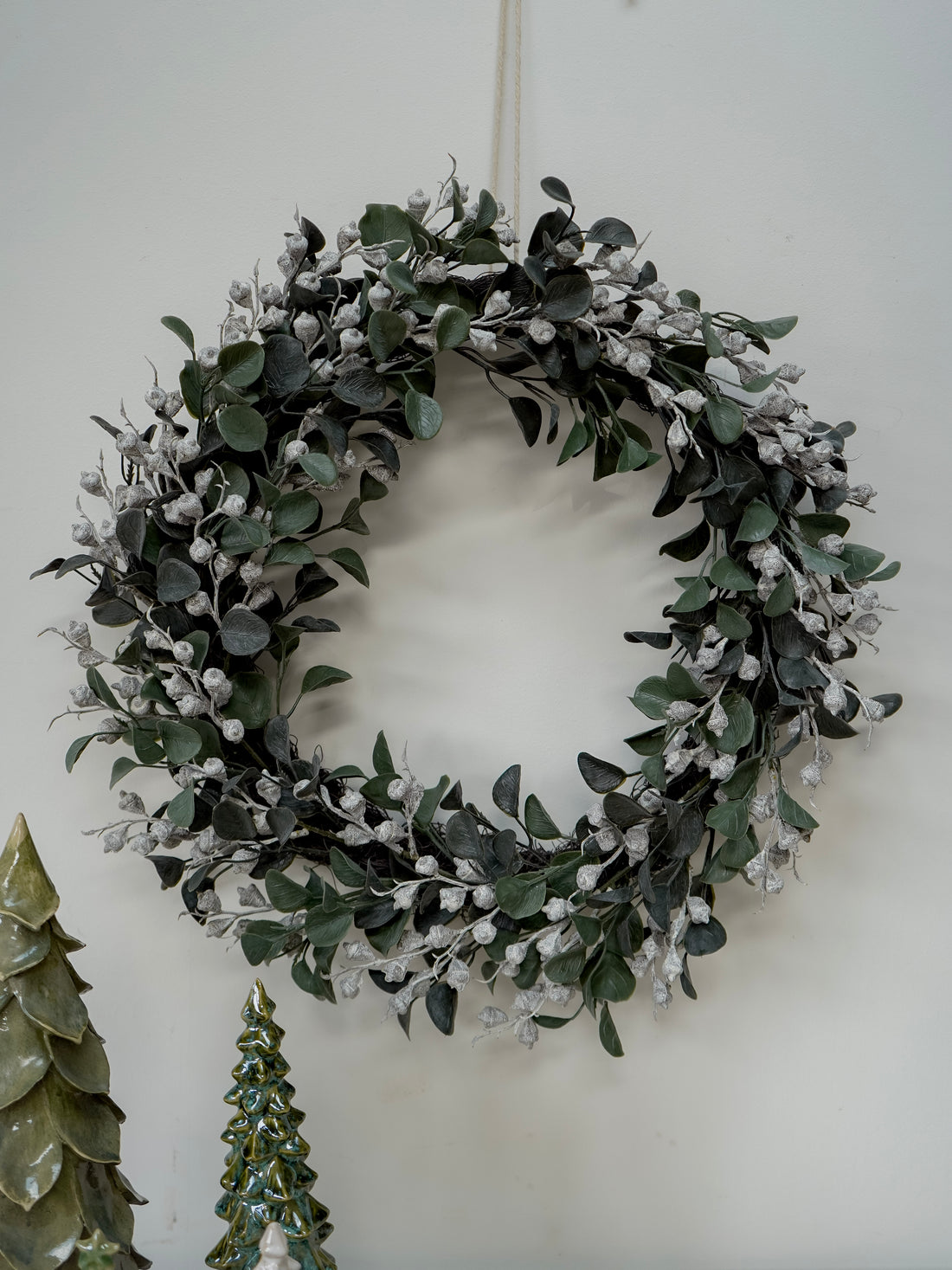 faux green foliage wreath with small white flowers on a white wall