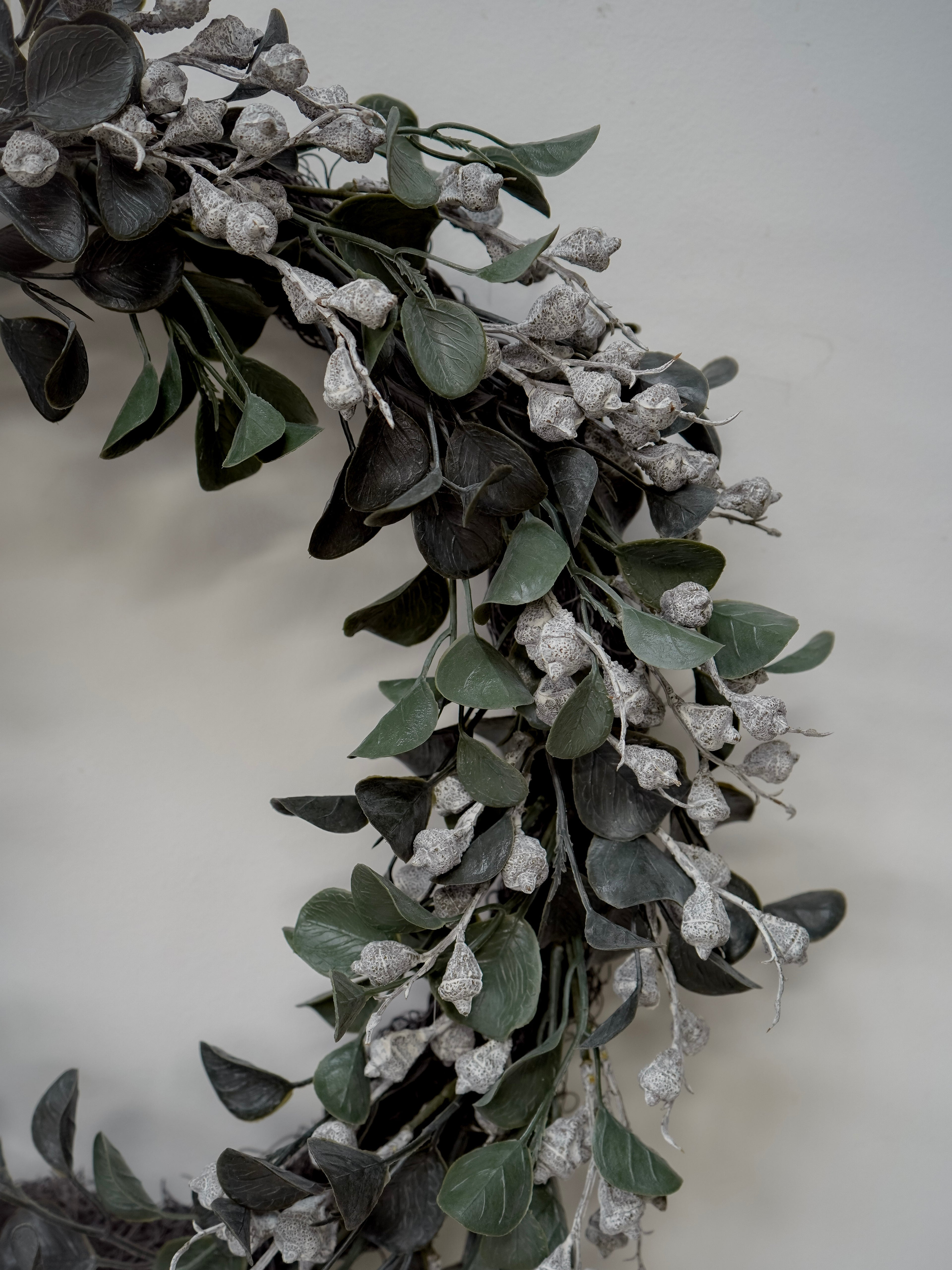 Decorative  faux christmas wreath with green leaves and small white flowers on a plain background