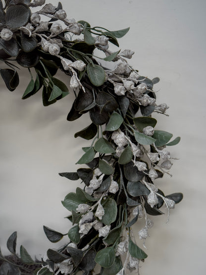 Decorative  faux christmas wreath with green leaves and small white flowers on a plain background