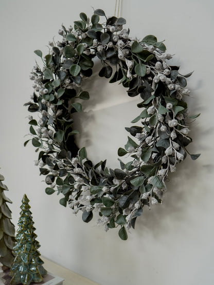 Green leafy wreath on a white wall with a small decorative tree in the corner.