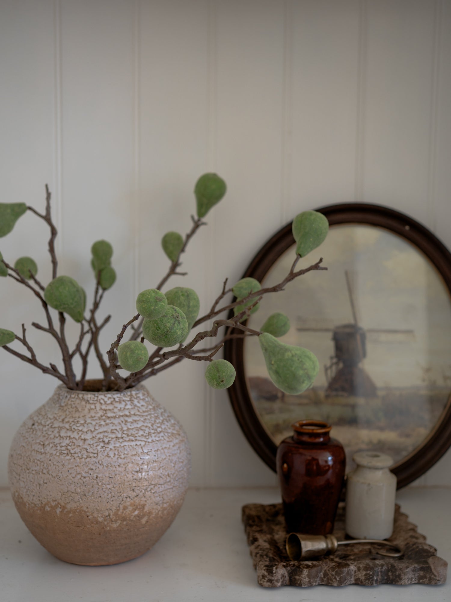 Decorative setup with a textured vase, green plant, and vintage photo on a white surface.