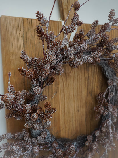 Decorative wreath with pinecones and branches on a wooden board