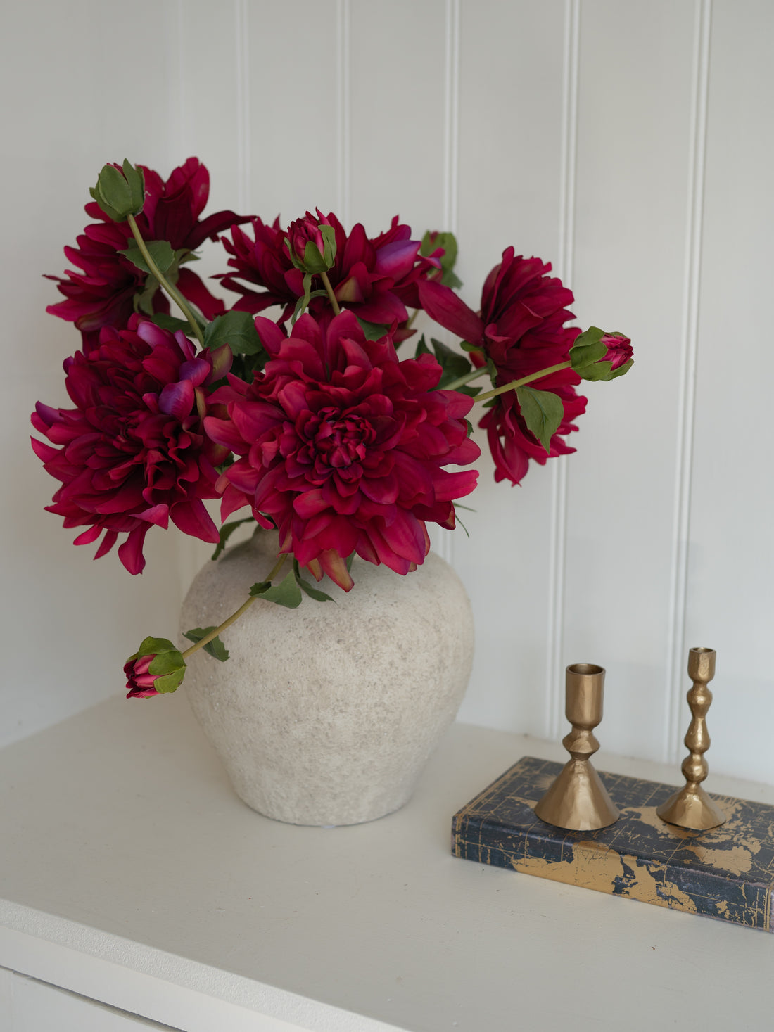 Vase with Faux Fuchsia Dahlia Stem flowers on a white surface with a white wall background