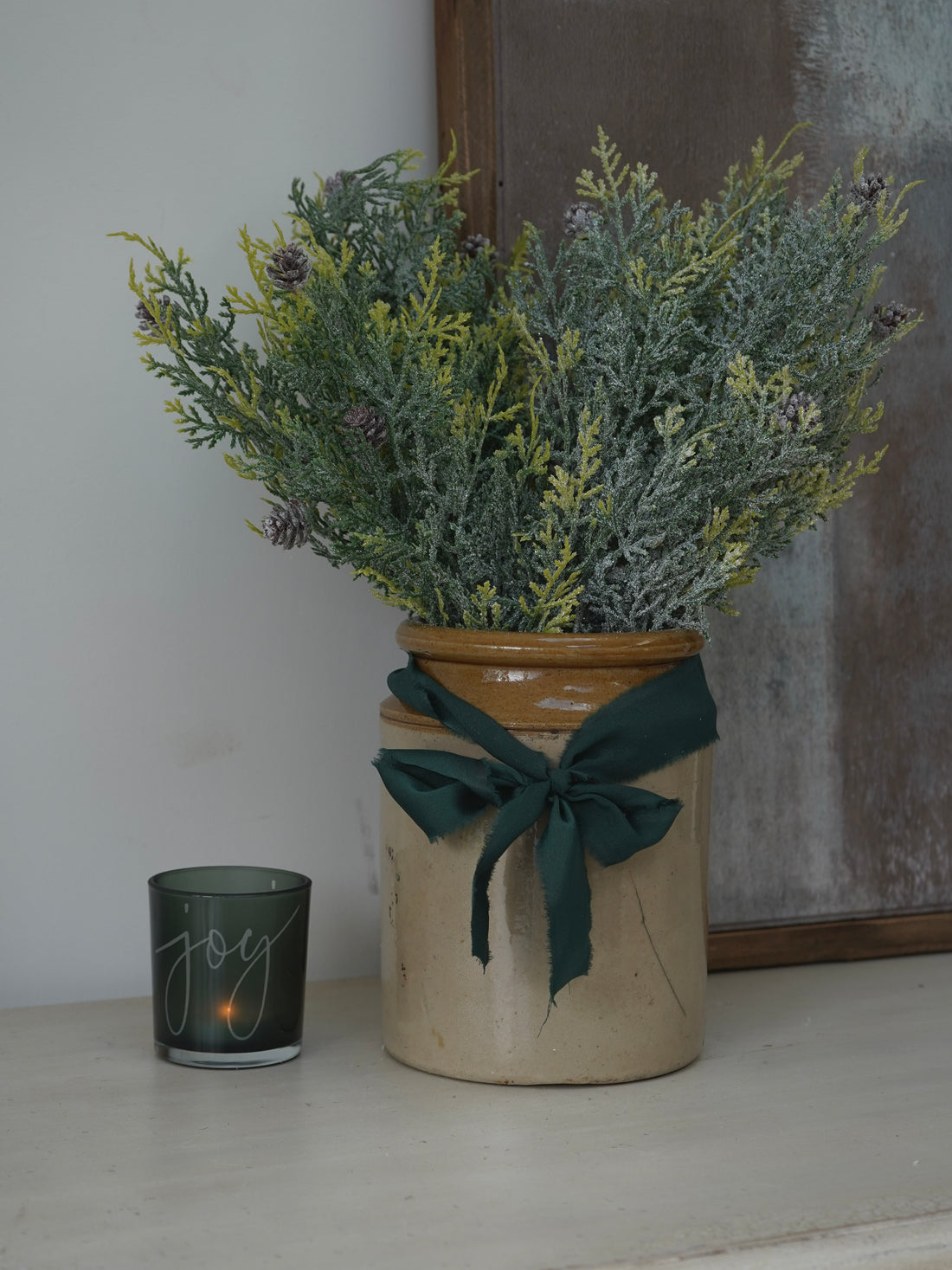 Decorative vase with Faux Glitter Pine Spray with Cones and a candle on a surface