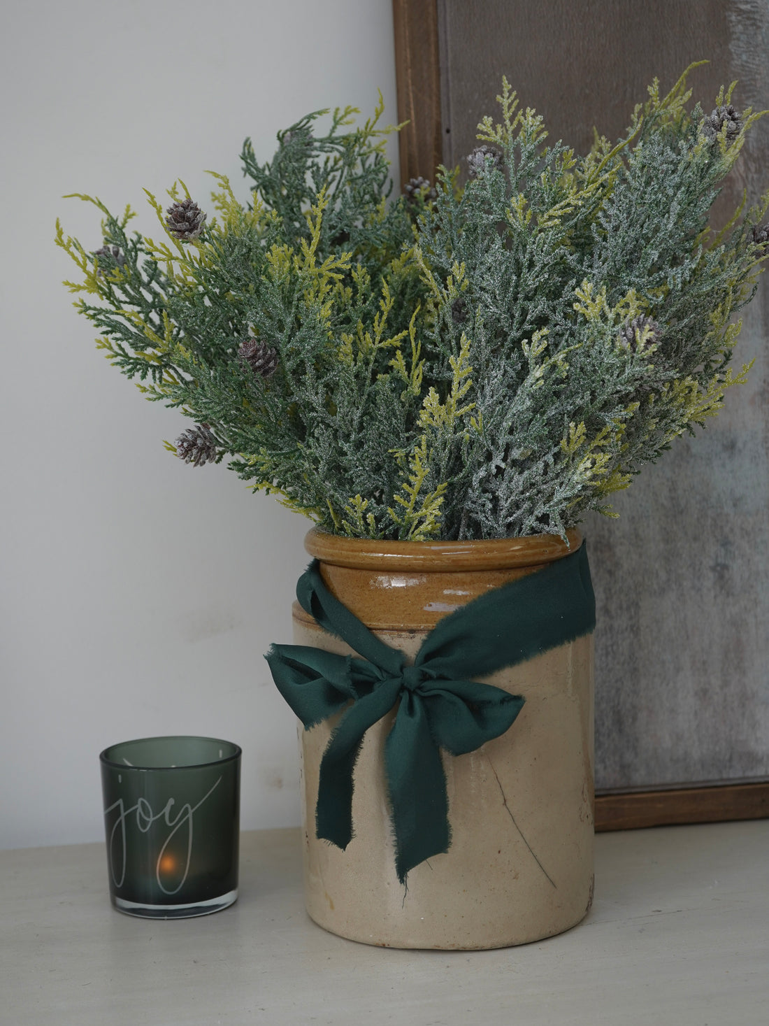Decorative pot with Faux Glitter Pine Spray with Cones and a candle labeled &