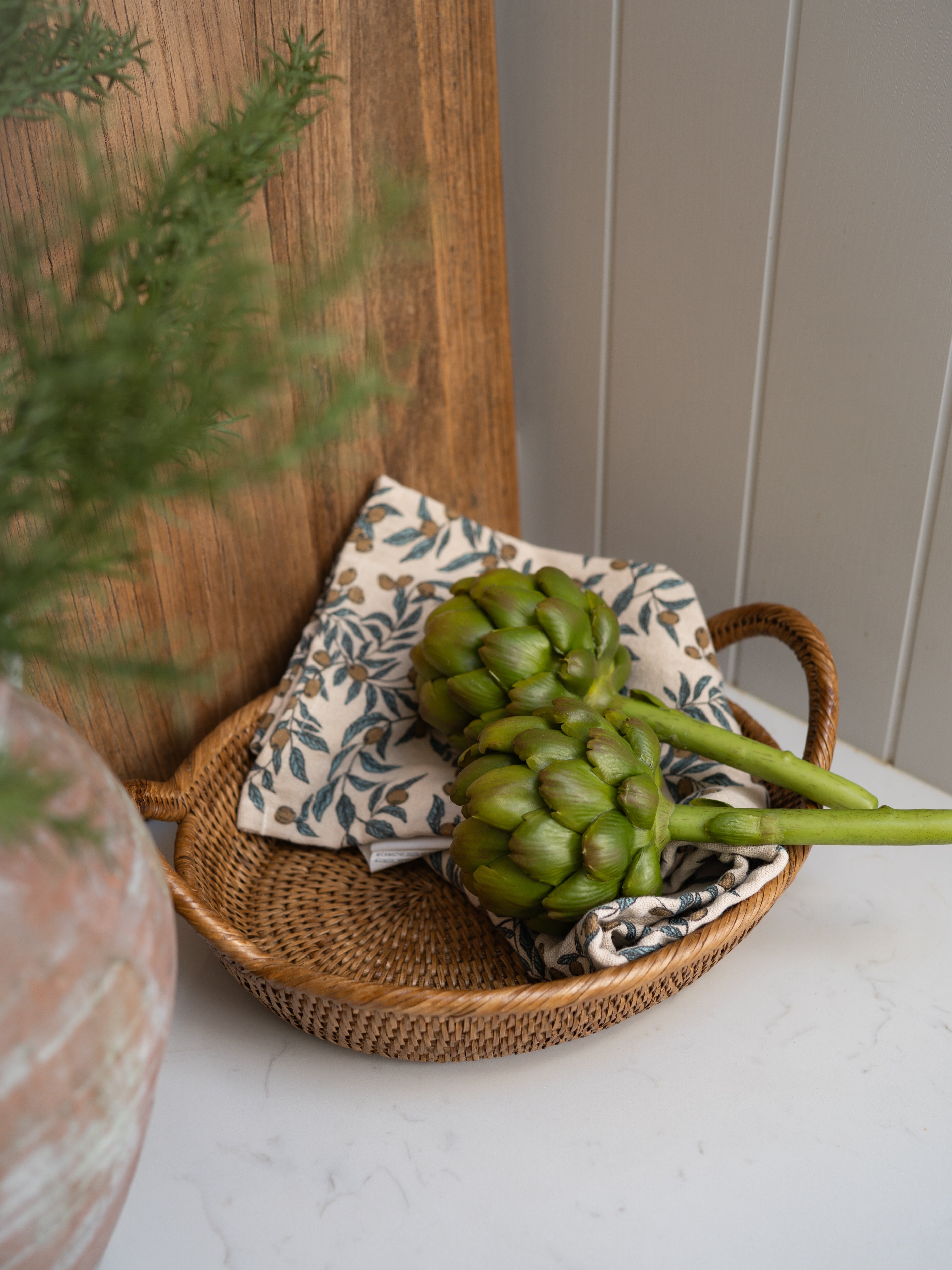 faux artichokes on a woven tray with a plant and wooden board in the background
