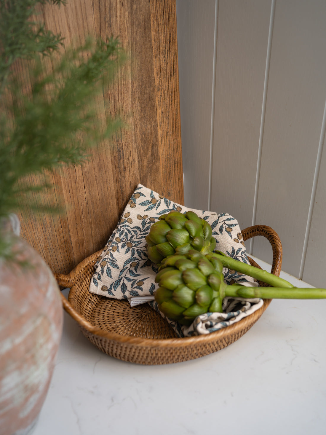 Faux artichoke in a woven basket with a decorative pillow on a wooden surface