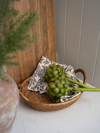 Faux artichoke in a woven basket with a decorative pillow on a wooden surface