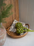 Faux artichoke in a woven basket with a decorative pillow on a wooden surface