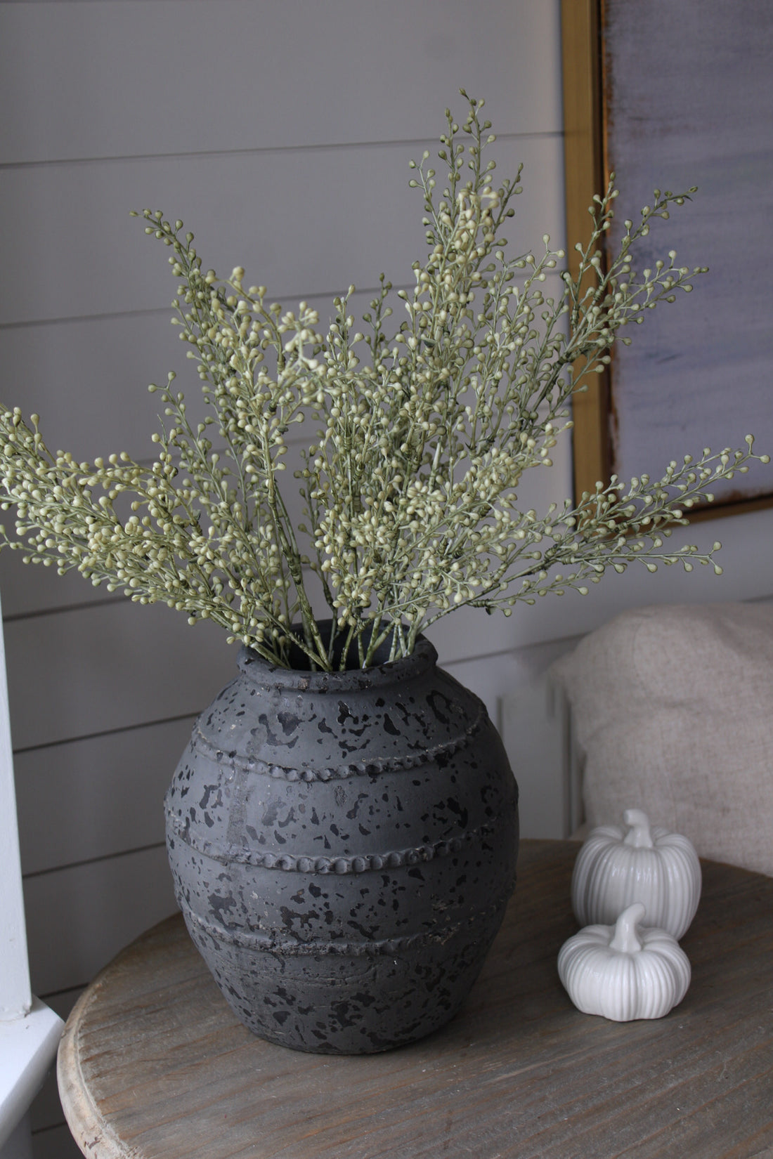 Decorative vase with faux autumn branches on a wooden table against a neutral wall.