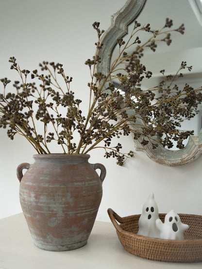 vintage style olive pot filled with faux huckleberry stems with rattan tray with decorative autumn ghost ornaments in the foreground