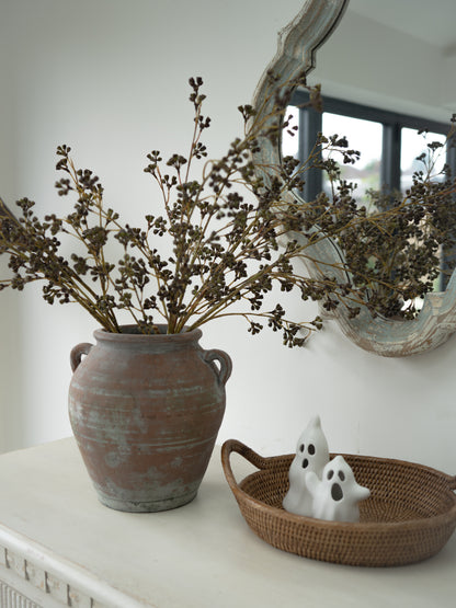 Artificial green and brown pod stems styled en masse in vintage olive pot