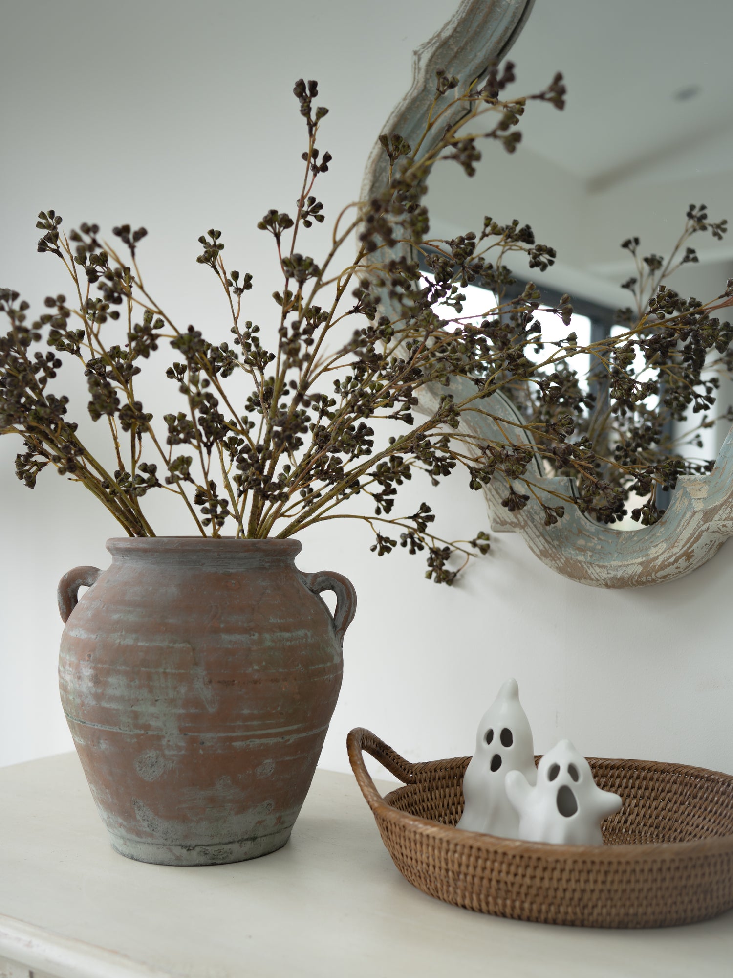 faux green huckleberry stems in vintage olive pot with oval rattan tray and white pair of ghost ornaments