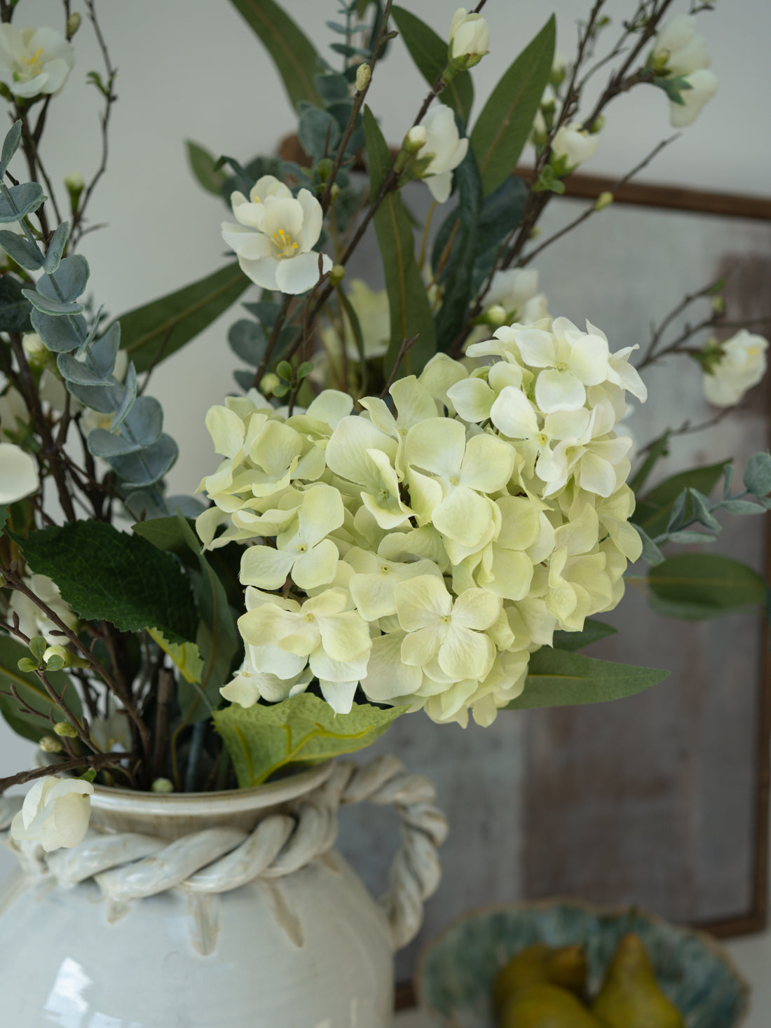 Decorative arrangement of faux flowers in a white vase with a blurred background