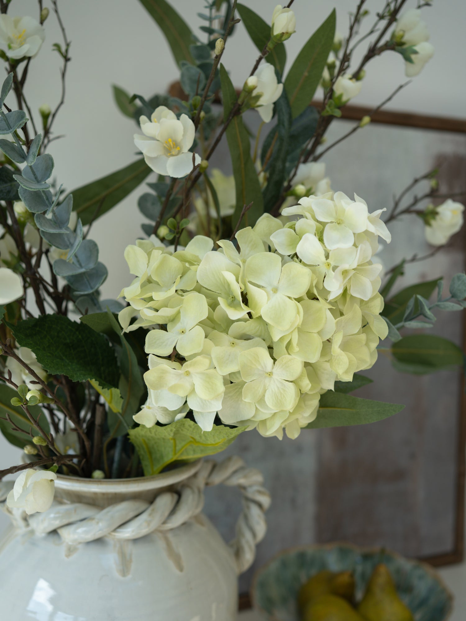 Decorative arrangement of faux flowers in a white vase with a blurred background