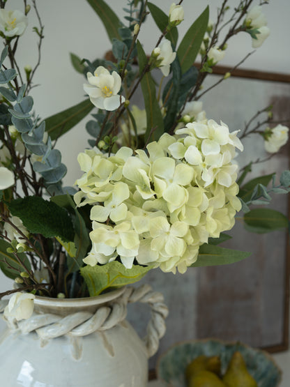 Decorative arrangement of faux flowers in a white vase with a blurred background