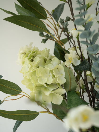 Arrangement of faux green and white flowers with leaves on a light background