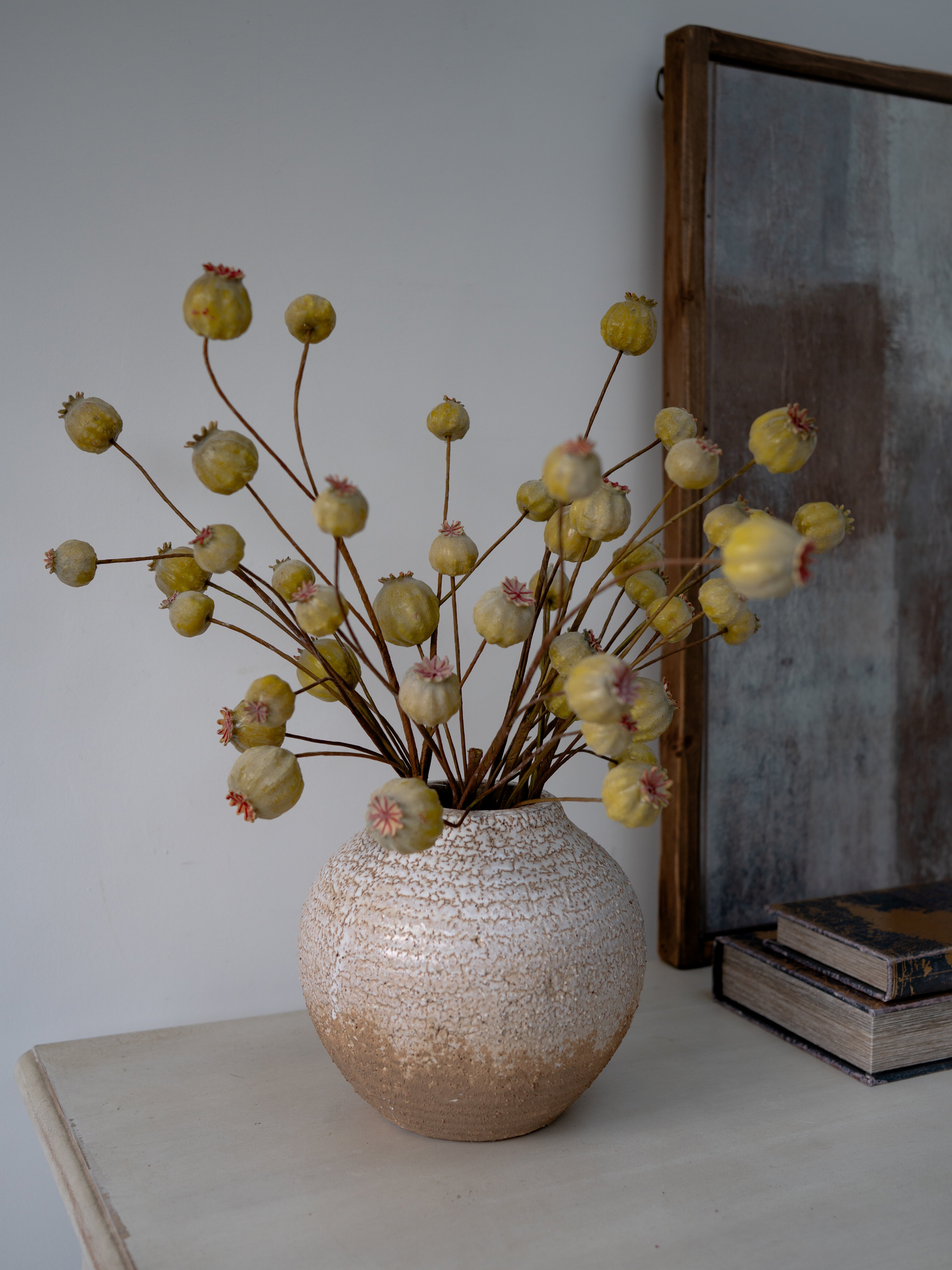 Decorative vase with faux green poppy head branch on a table next to a mirror