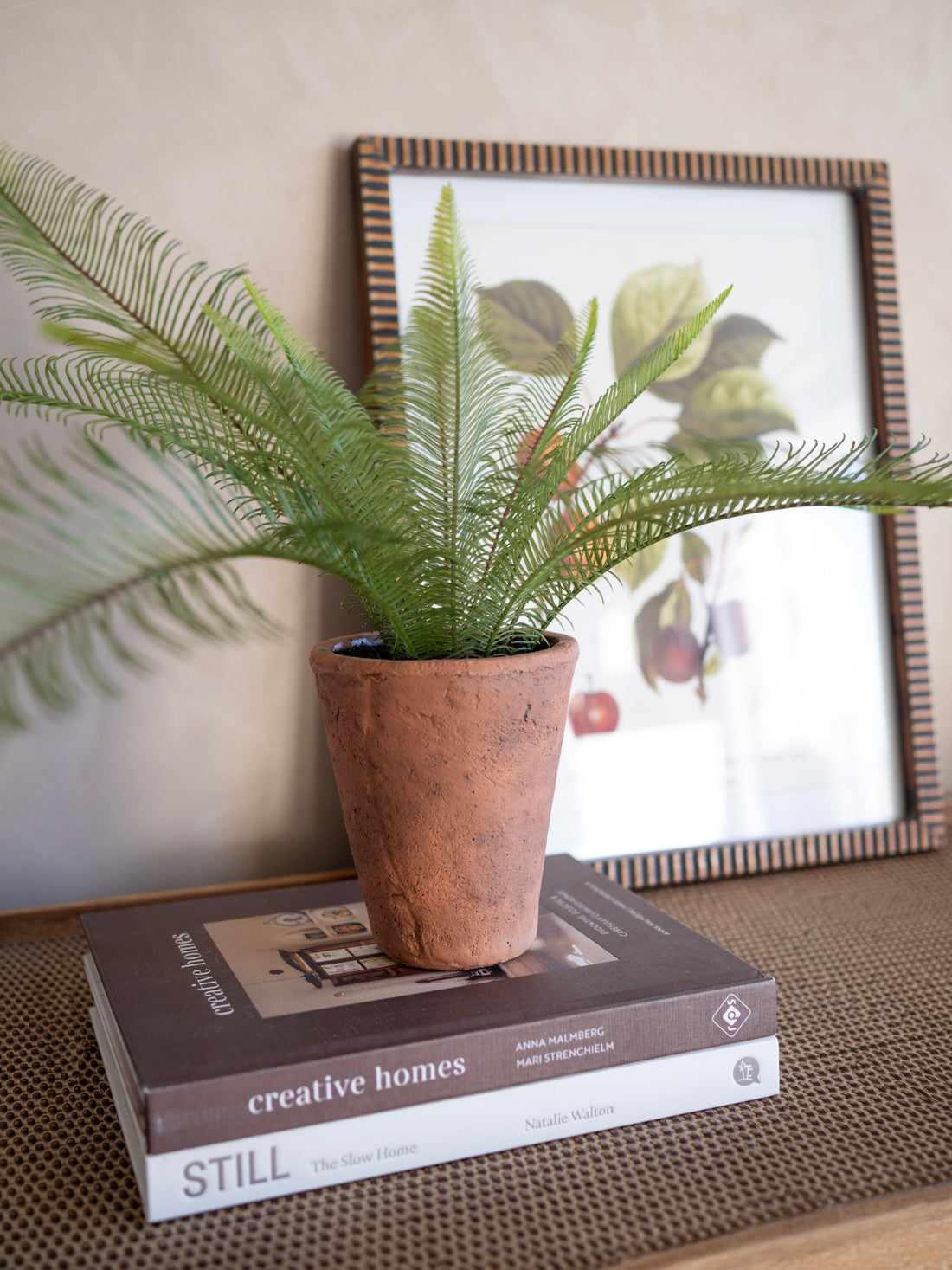 Potted faux java fern plant on a book with a framed picture in the background