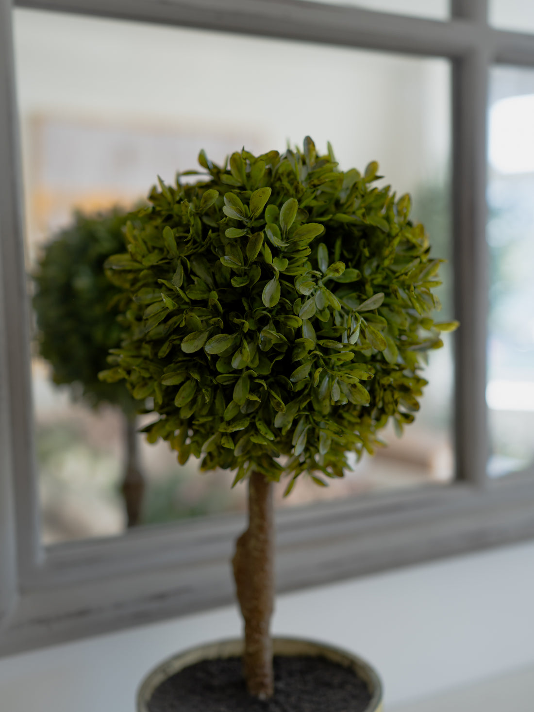 Artificial topiary tree in a pot on a windowsill with a blurred window background