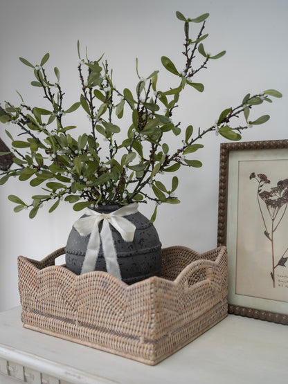 Decorative arrangement with a vase of greenery in a woven basket on a white surface.