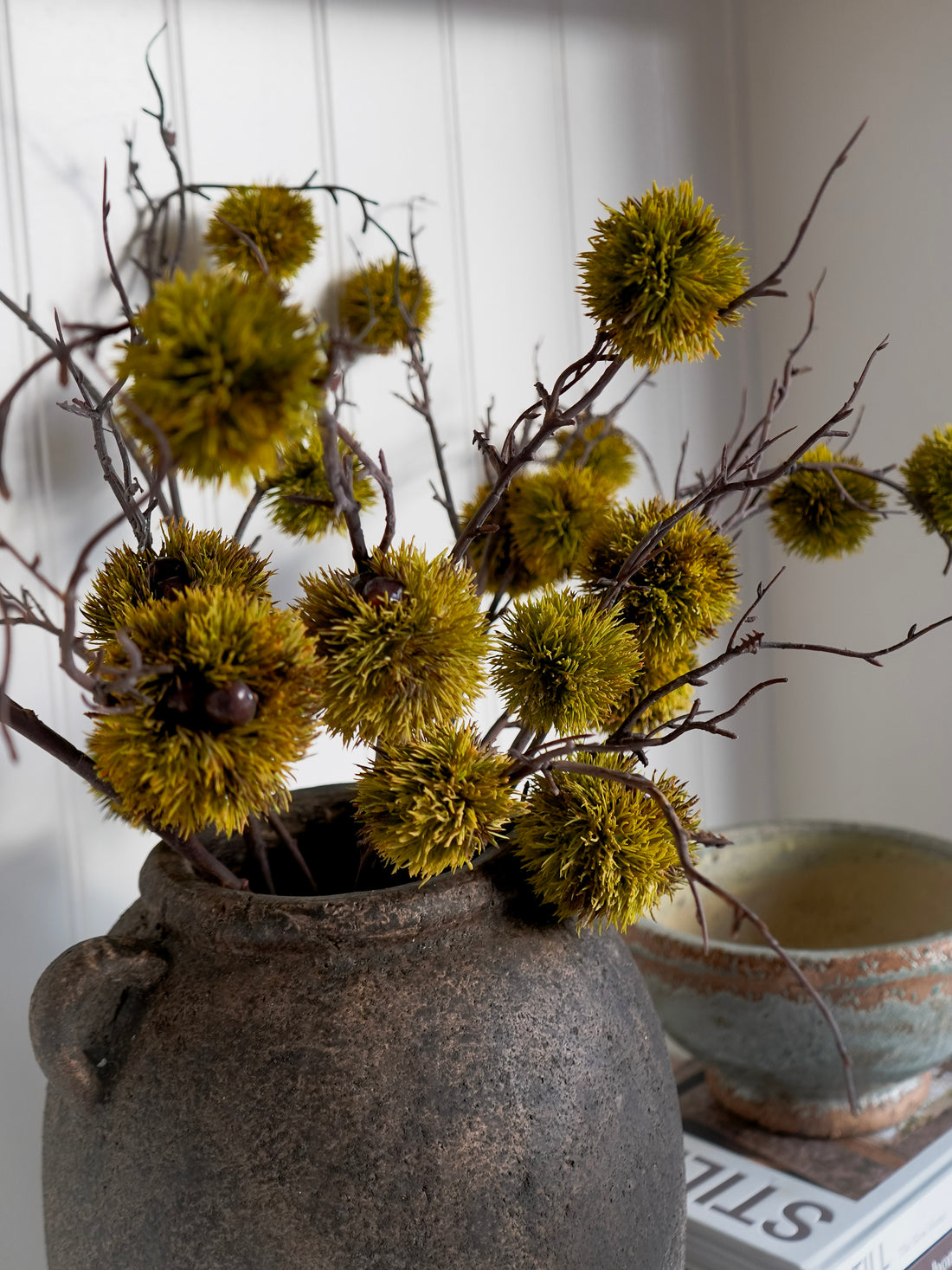 Decorative faux moss chestnut with in a textured vase on a white surface.