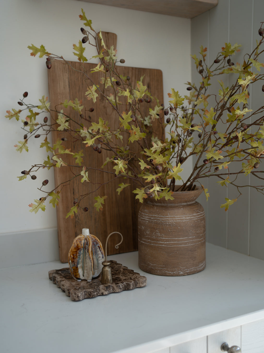 Decorative faux oak and acorns branch arrangement with a vase, branches, and small vase on a shelf.
