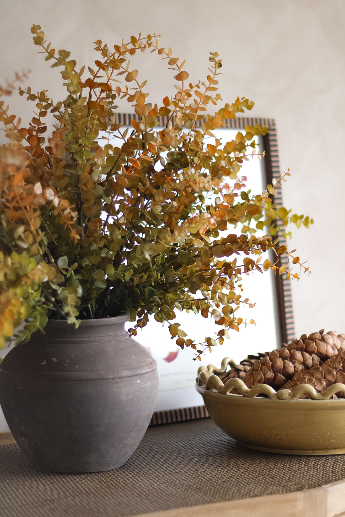 Autumn decorative arrangement with a potted plant and a bowl of pinecones on a surface.